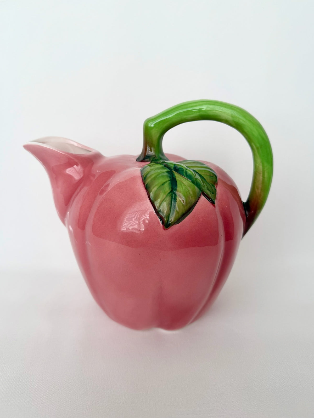 Vintage glazed ceramic apple pitcher with green handle detail.