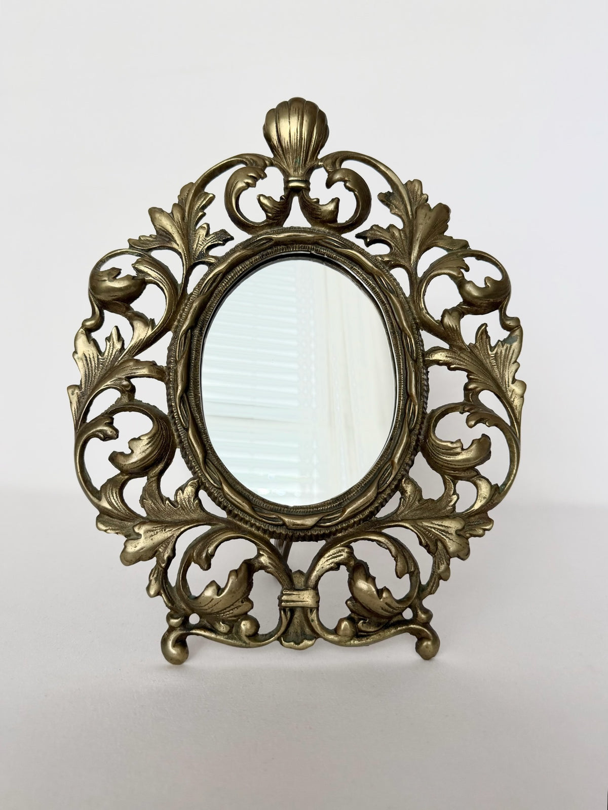 Vintage brass table top mirror with swirly acanthus leaves design and kick stand in back.