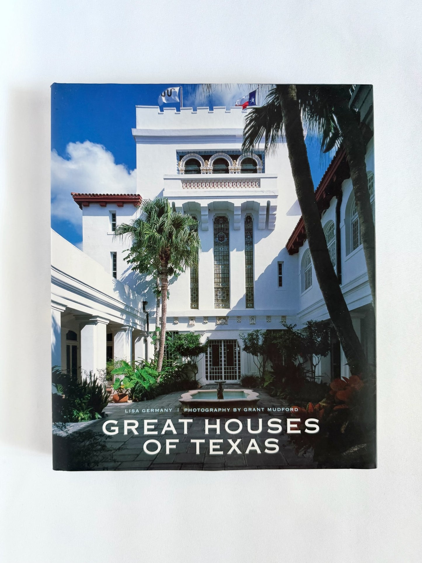 A hardcover book titled 'Great Houses of Texas' standing upright against a plain white background. The cover features a photograph of a white historic house with palm trees under a blue sky.