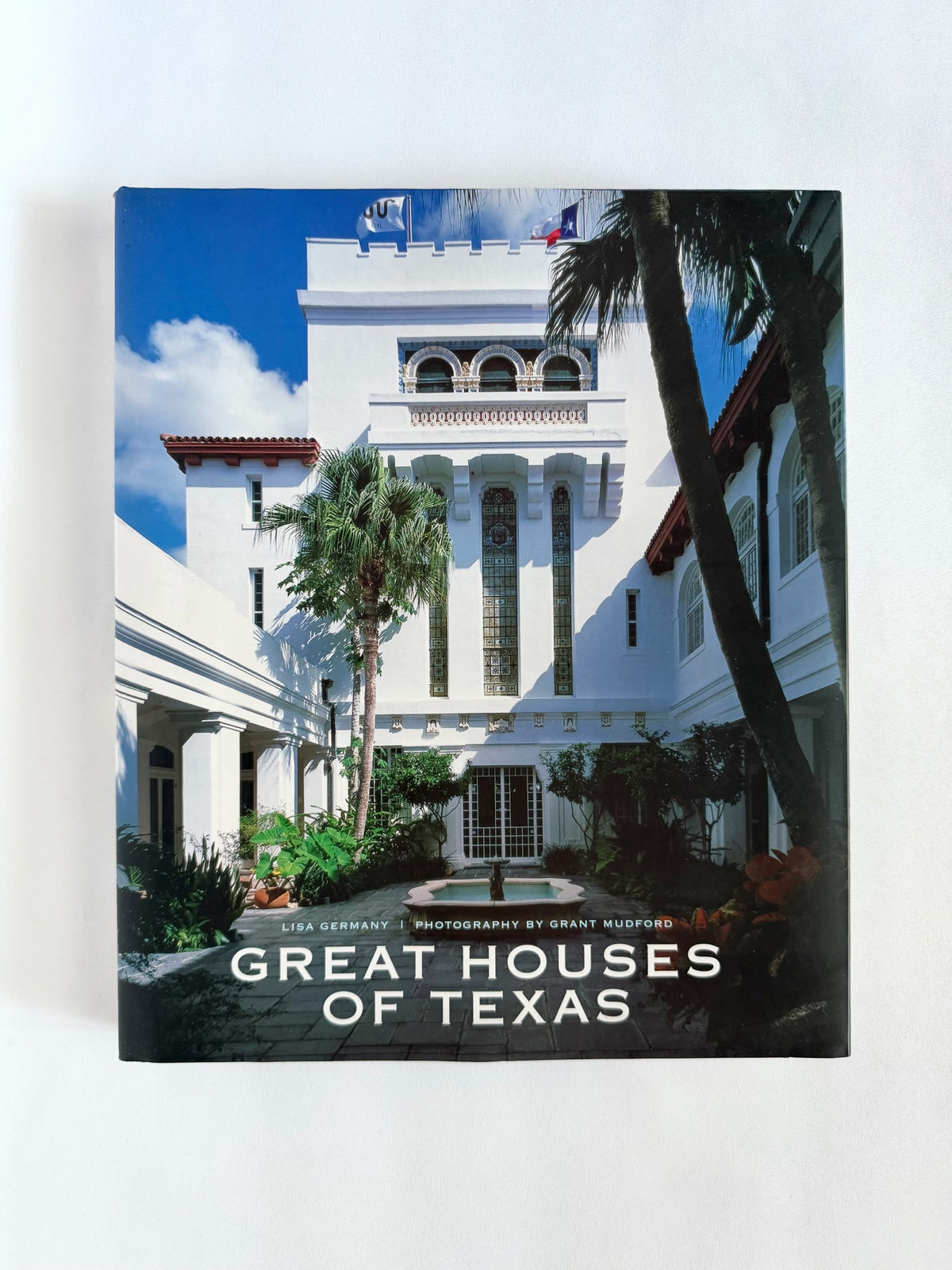 A hardcover book titled 'Great Houses of Texas' standing upright against a plain white background. The cover features a photograph of a white historic house with palm trees under a blue sky.