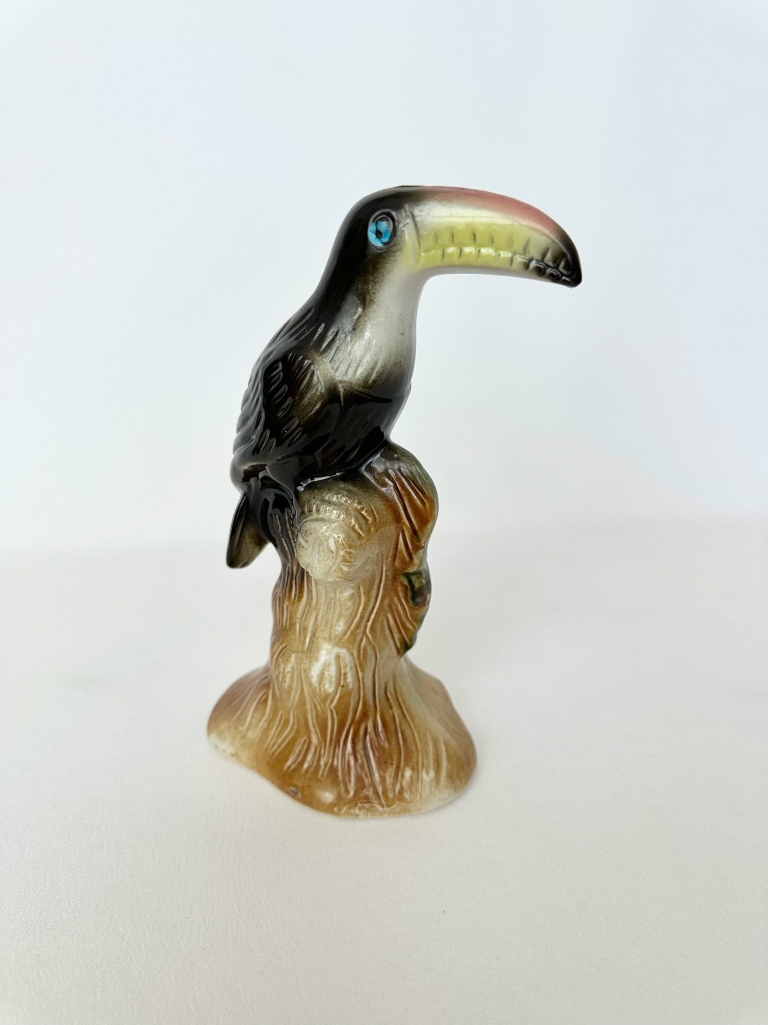 vintage ceramic toucan figurine on a tree stump in black, yellow and cream with a blue eye