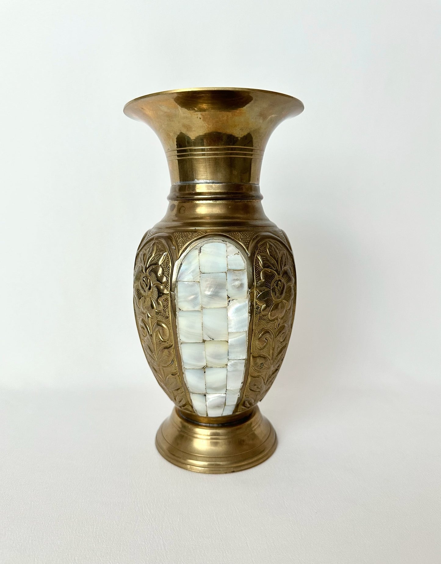 A vintage brass vase with a flared rim, ornate floral engraving, and  inlay of white mother-of-pearl shell tiles