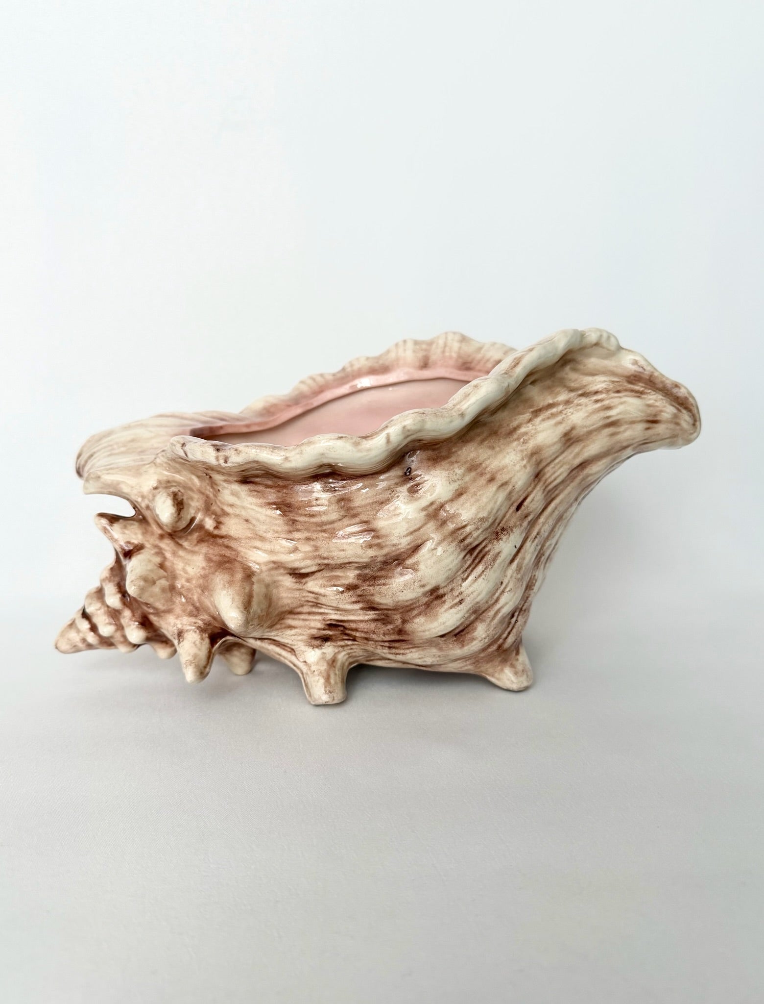 A vintage decorative ceramic shell-shaped planter with a realistic conch shell design, featuring a textured brown and beige pattern with a soft pink interior