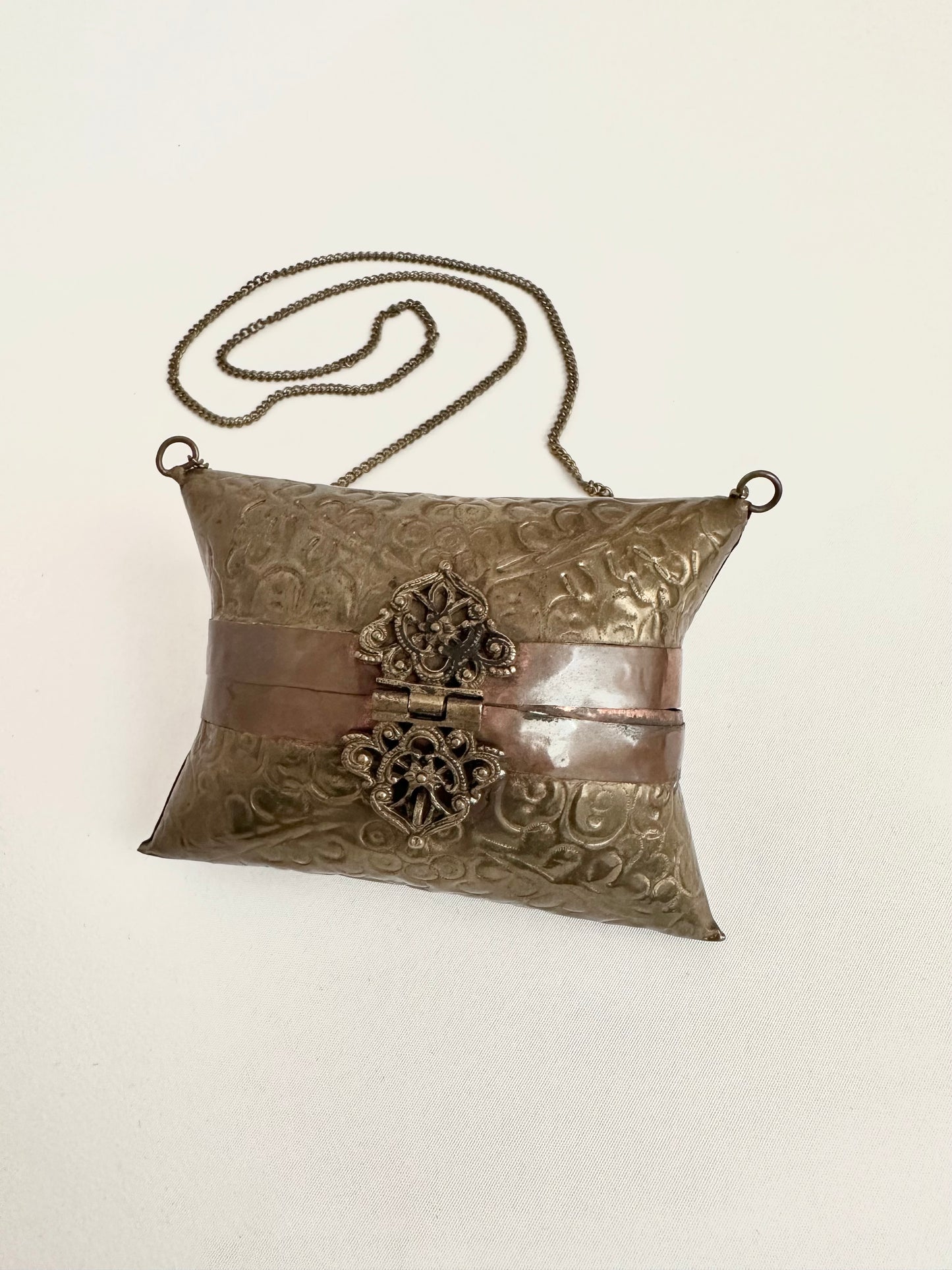 Vintage brass embossed pillow purse with ornate latch on a chain strap