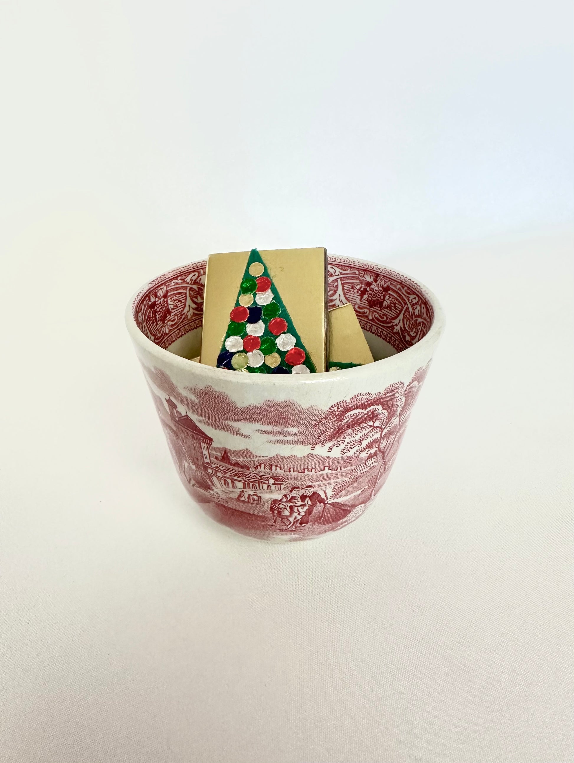 Red transferware cup with countryside scenery paired with a set of four vintage christmas matchboxes.
