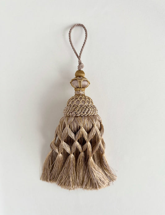A decorative tassel ornament with a braided beige taupe cord body, a gold-toned top cap, and a hanging loop,