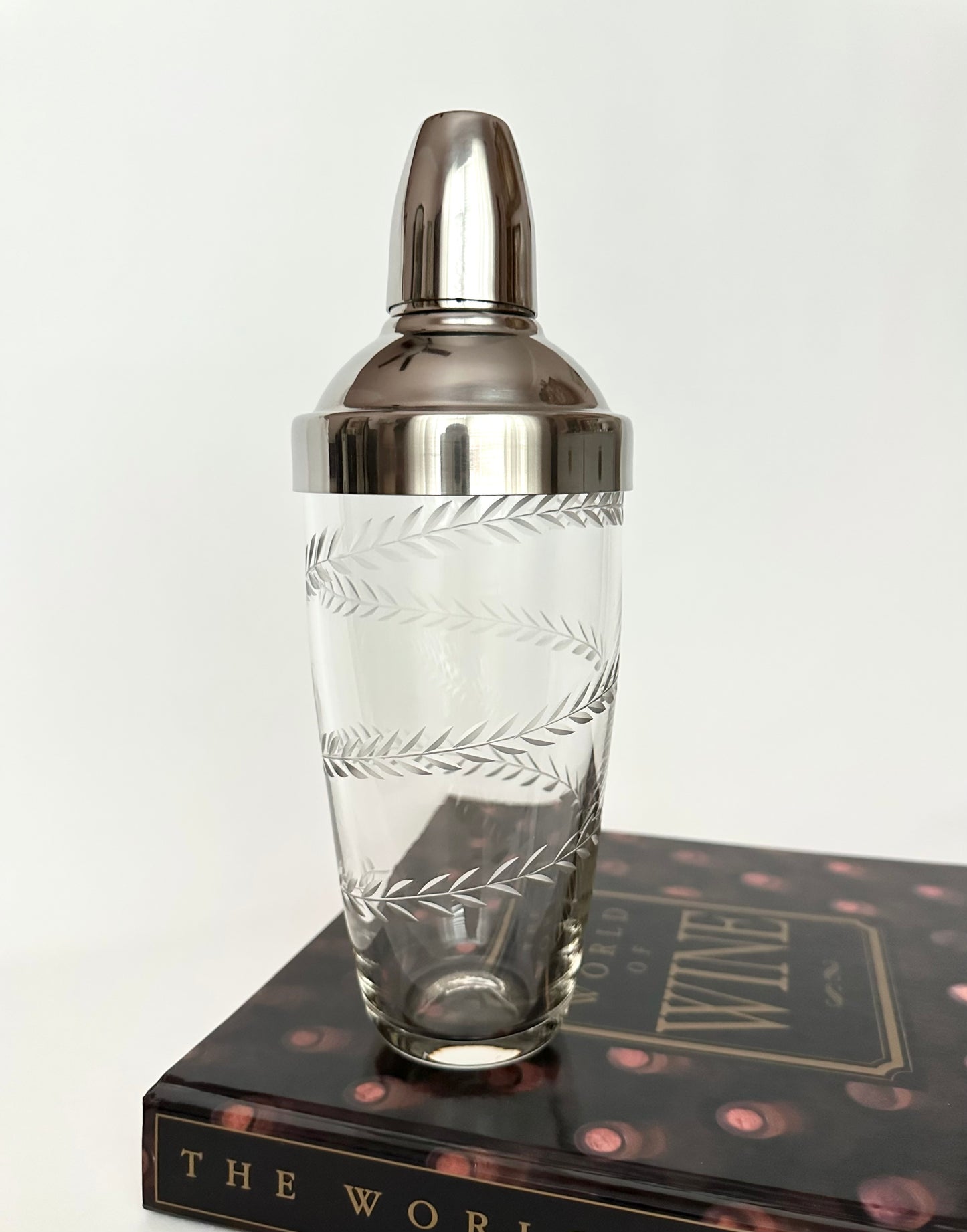 Vintage glass and stainless steel cocktail shaker with etched laurel leaf pattern.