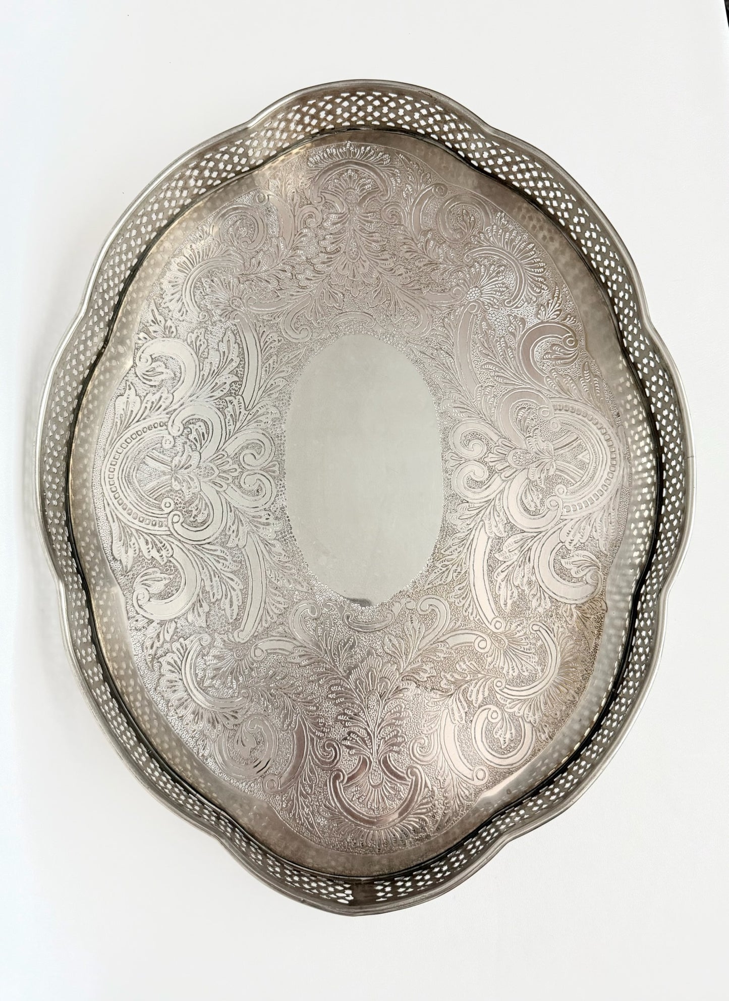 A vintage oval silver serving tray with a decorative pierced border and an etched floral scroll pattern