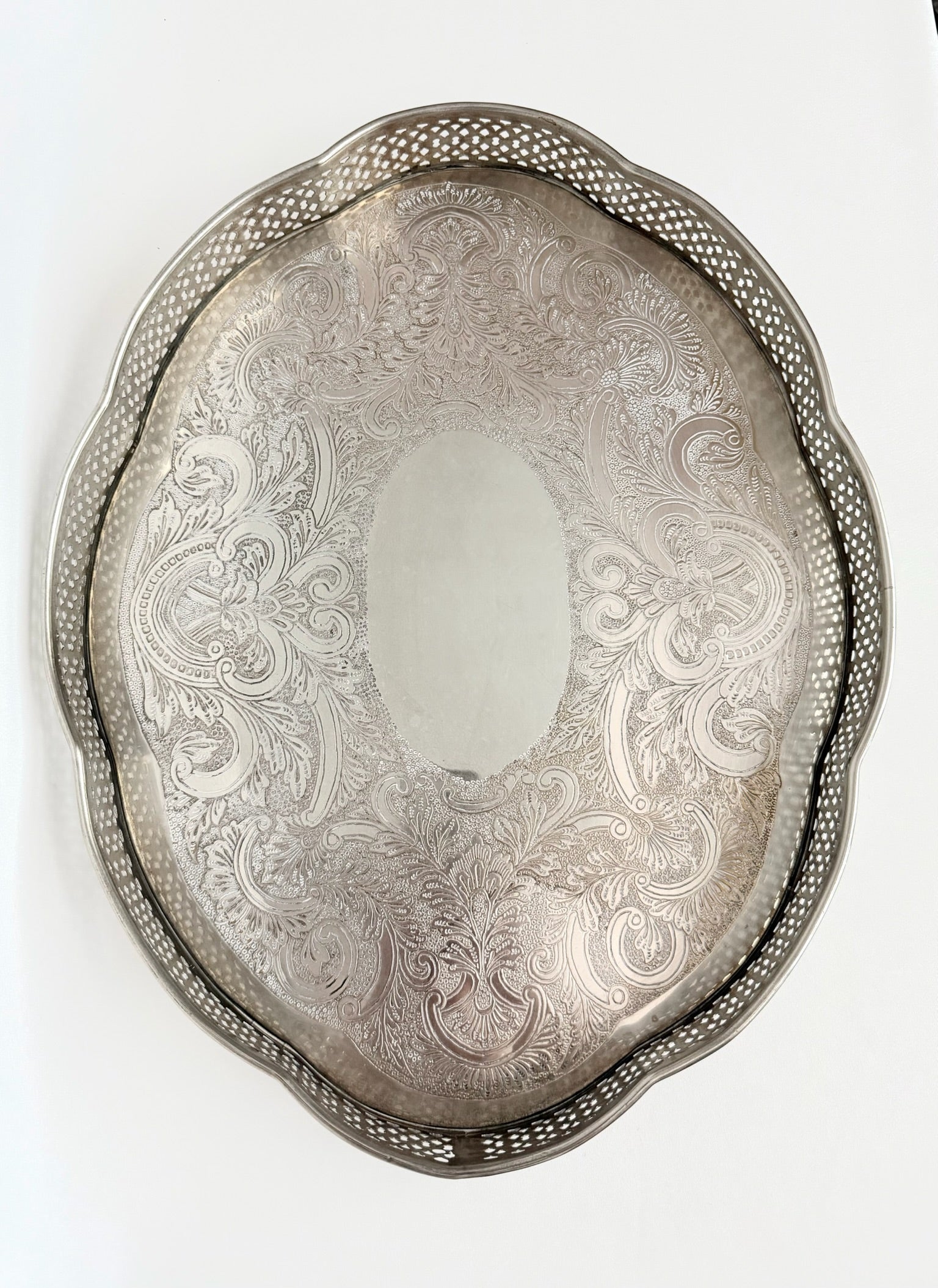 A vintage oval silver serving tray with a decorative pierced border and an etched floral scroll pattern