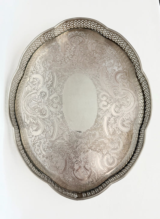 A vintage oval silver serving tray with a decorative pierced border and an etched floral scroll pattern