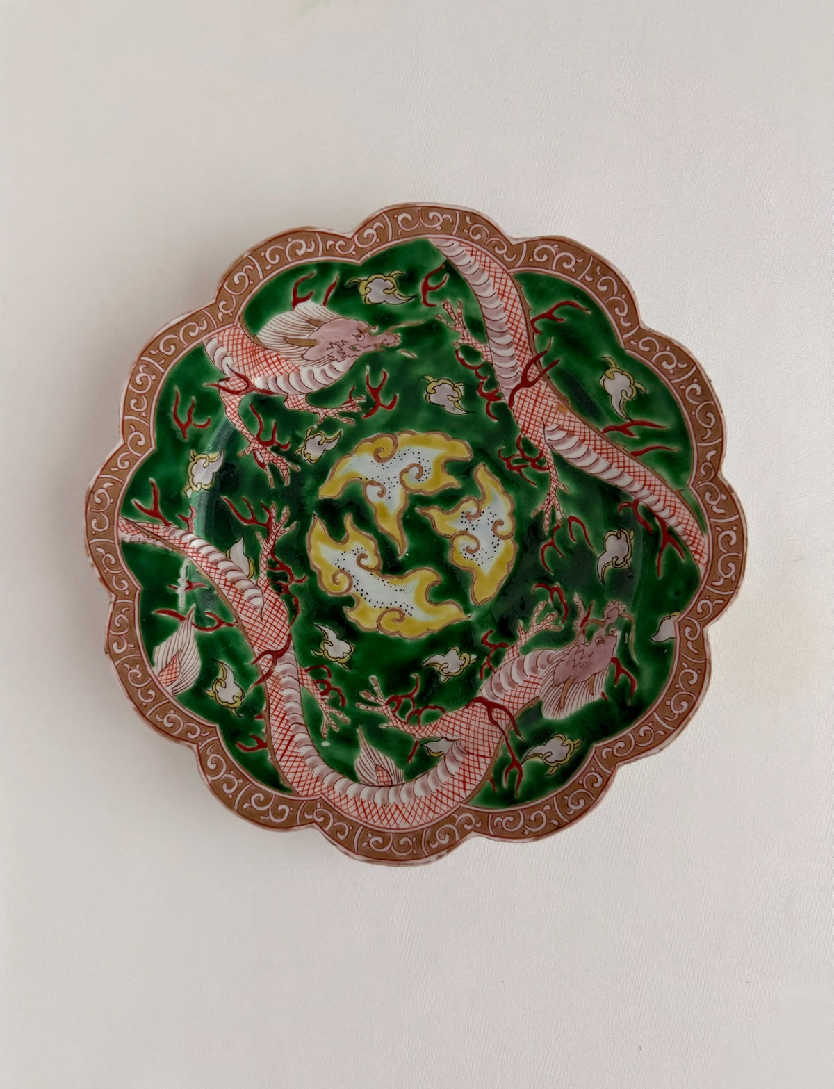 Vintage or antique scalloped chinoiserie decorative plate with dragons in reds, greens and yellows.