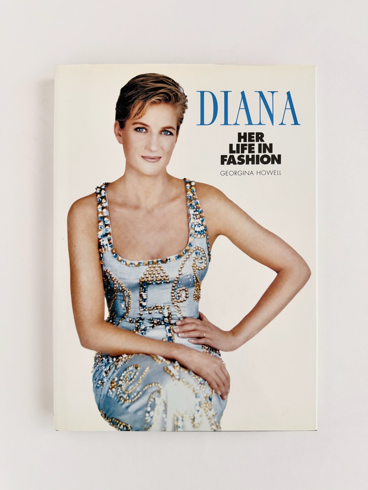 Vintage copy of 'Diana: Her Life in Fashion' by Georgina Howell, featuring a portrait of Princess Diana in a patterned light blue dress against a cream background.