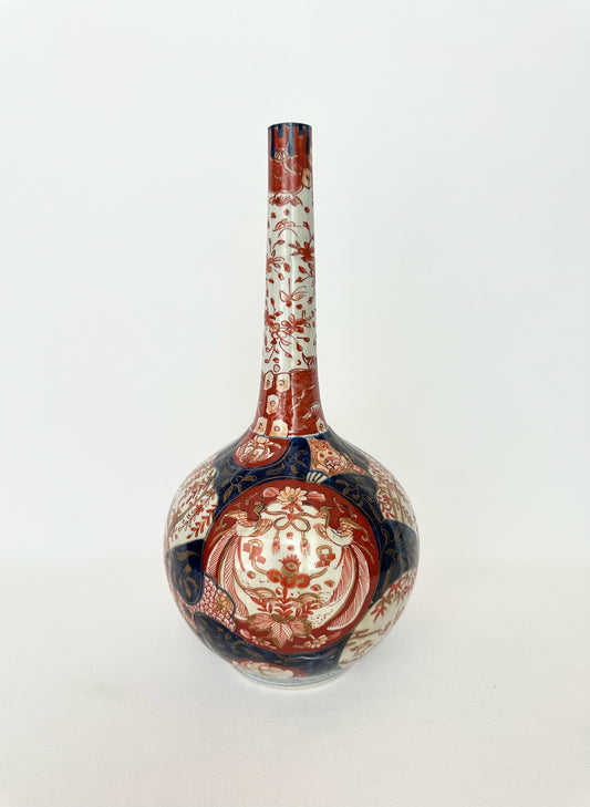 An antique Japanese Imari porcelain vase with a long neck and bulbous base, decorated with red and navy blue floral patterns 